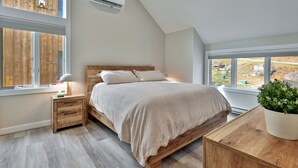Et soveværelse med en træseng, et natbord, en sengetavlelampe, en potteplante og udsigt til det fri gennem vinduet.