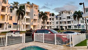 A multi-story hotel with balconies, a swimming pool, and parked cars. - Surfside Beach Condo in wonderful Aguada, PR (Aguada)