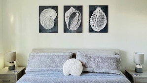 A bedroom with a bed, a ceiling fan, and three wall-mounted artwork pieces. - Surfside Beach Condo in wonderful Aguada, PR (Aguada)