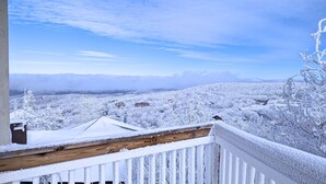 A snow-covered landscape with a wooden balcony railing and a view of houses and trees. - Classic | Ski-in/Out | Views | PetFriendly | 2BR (Beech Mountain)