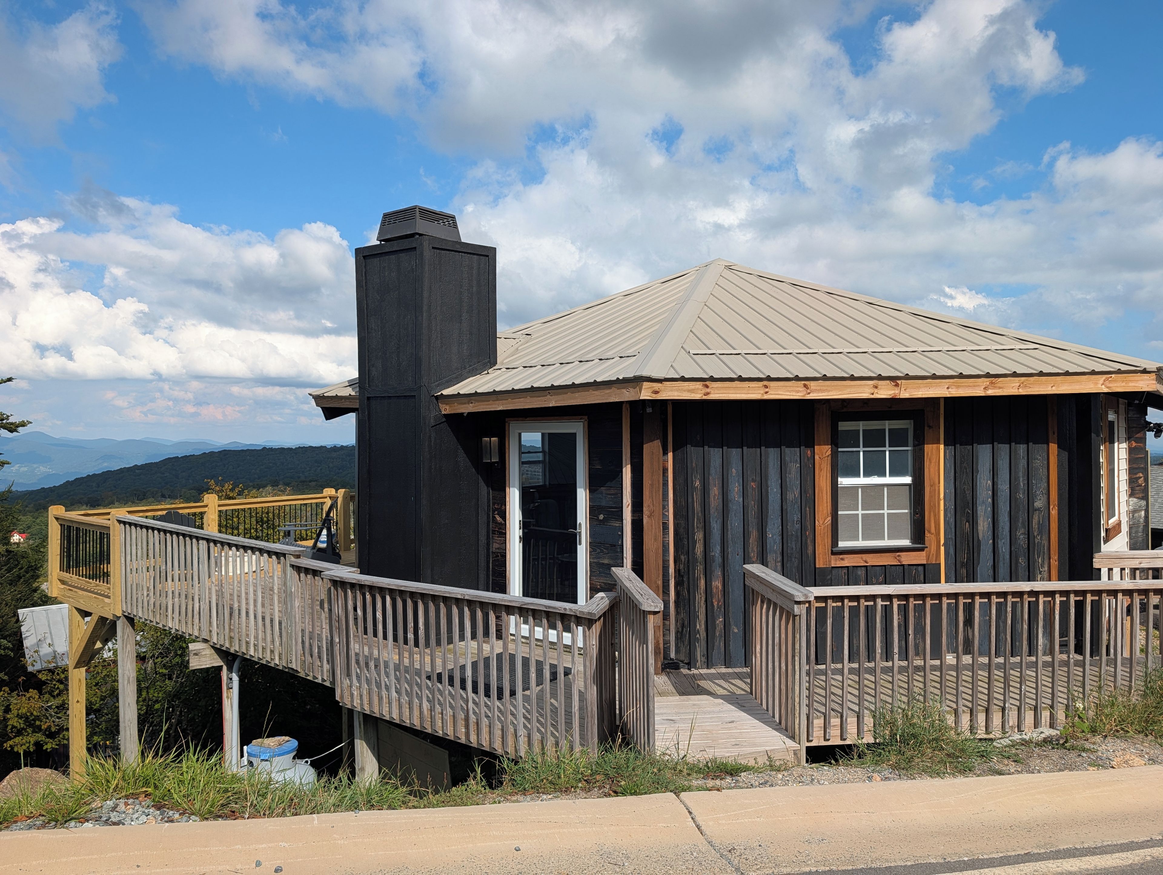 A rustic cabin with a wooden deck and a chimney, surrounded by a natural landscape.