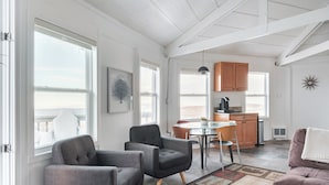 A spacious living area with a dining table, two armchairs, and a sofa. A kitchen is visible in the background with wooden cabinets and a hanging pendant light. - Classic | Ski-in/Out | Views | PetFriendly | 2BR (Beech Mountain)