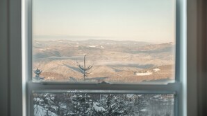 A view through a window of a mountainous landscape with snow-covered trees and distant buildings. - Classic | Ski-in/Out | Views | PetFriendly | 2BR (Beech Mountain)