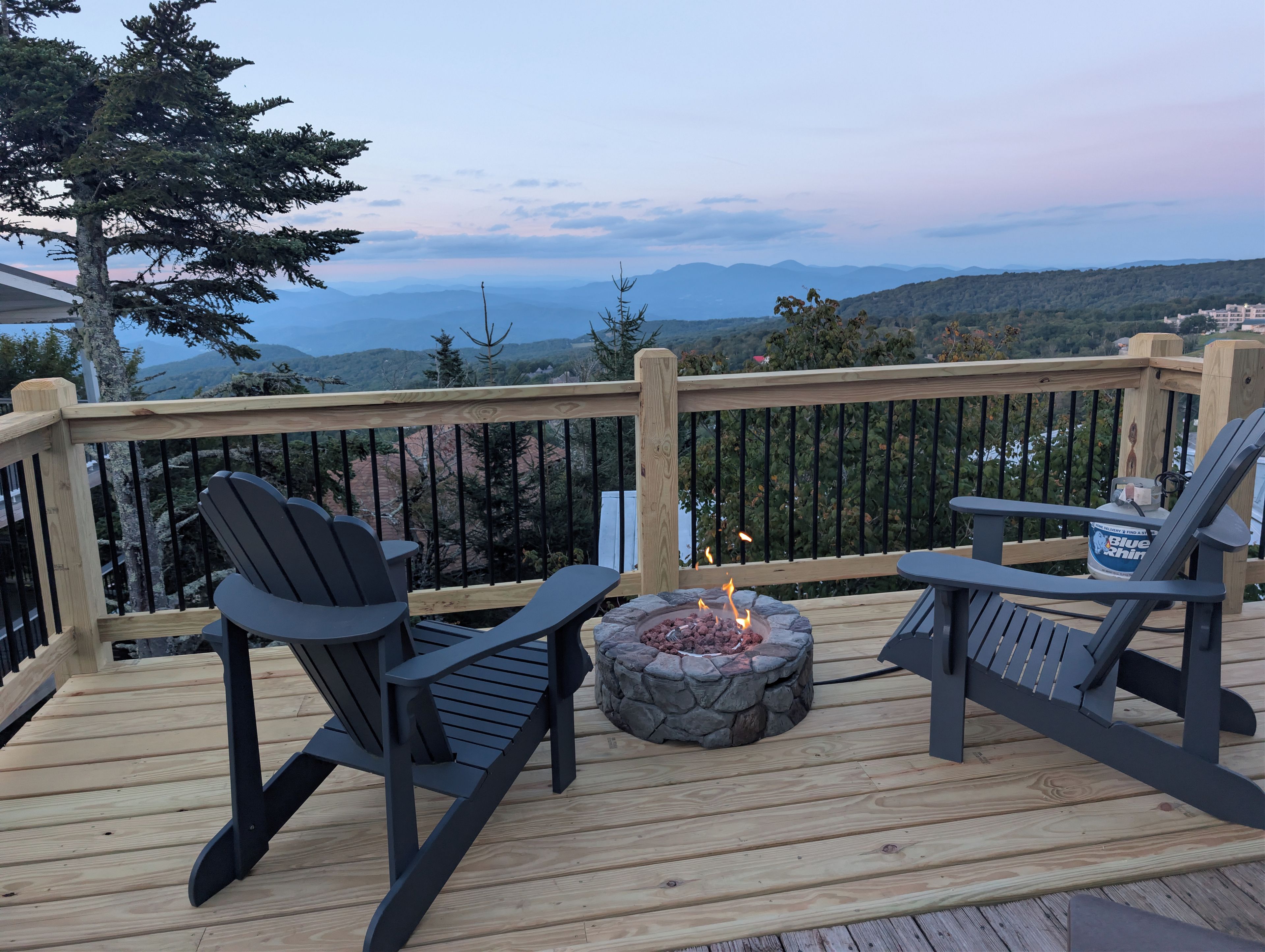 A deck with two Adirondack chairs, a stone fire pit, and a view of mountains.