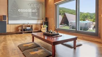 Una habitación acogedora con un ventanal grande, una mesa de madera y una pantalla de proyector que muestra la palabra 'essential'.
