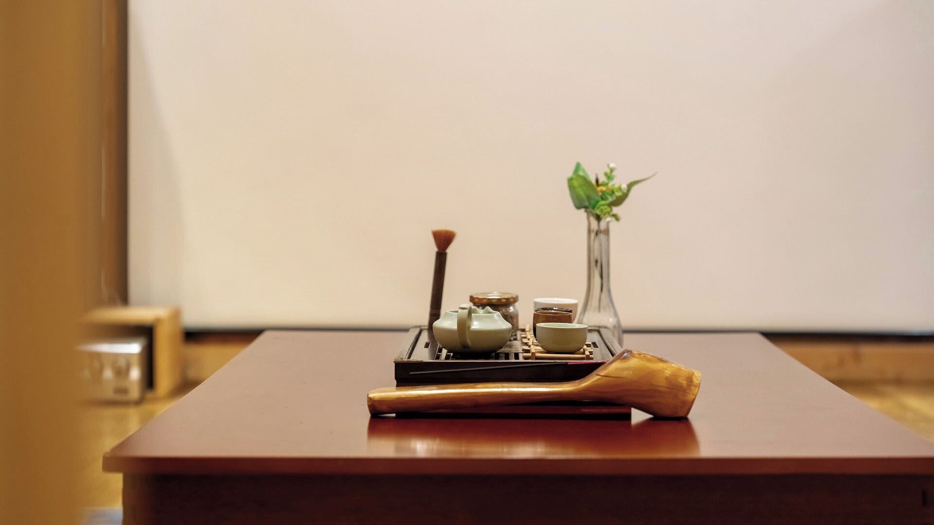 A traditional tea set on a wooden table with a wooden spoon, a tea brush, and a vase with a plant.