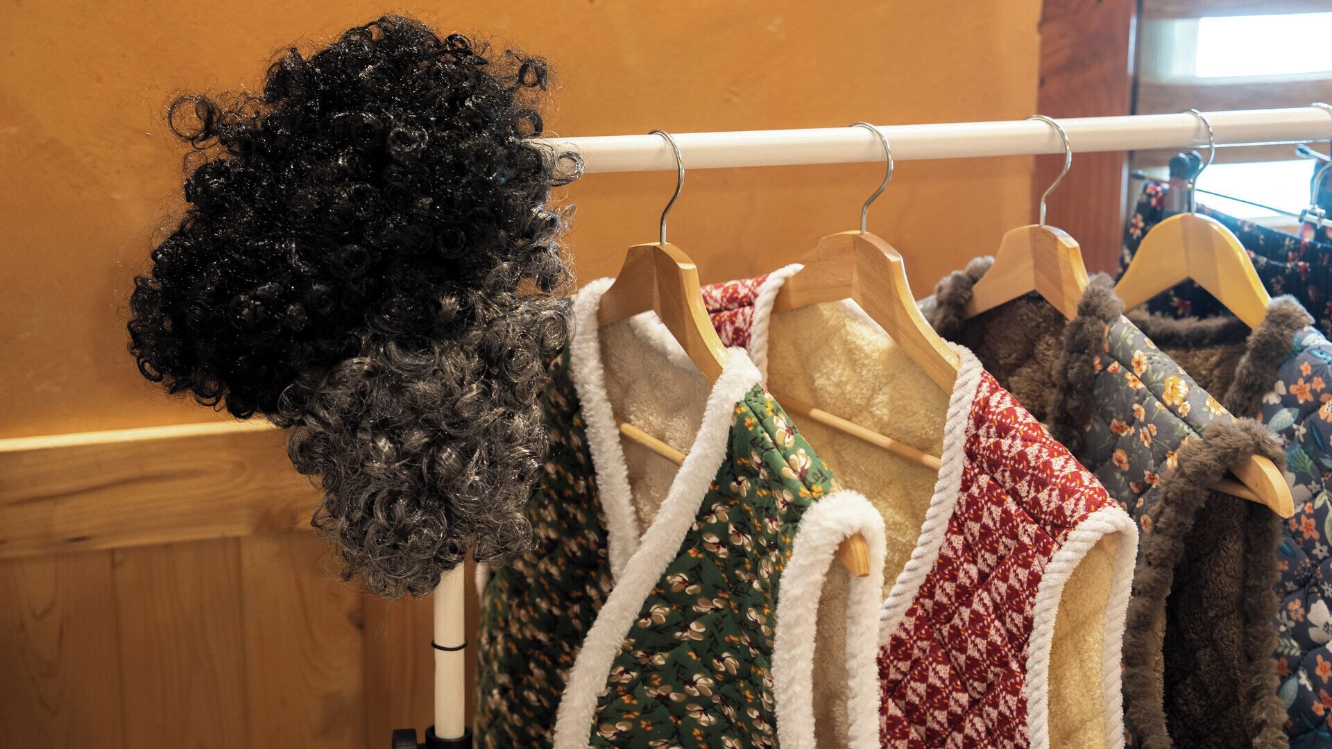 A rack of clothing items, including a variety of sweaters and a wig.