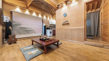 Una sala de estar acogedora con piso de madera, una mesa de centro, una guitarra y una pantalla de proyector.