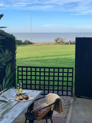 A patio with a table set for dining, overlooking a grassy area and the sea. - Westgate | Spectacular Sea Views | Log Burner | Sandy Beach 2 mins walk (Westgate on Sea)