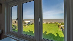 A room with three large windows overlooking a grassy area and a body of water.