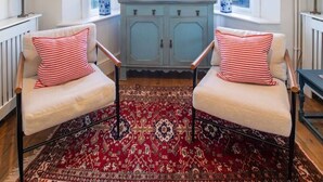 A room with a bay window, two armchairs with striped cushions, a patterned rug, and a light blue cabinet.