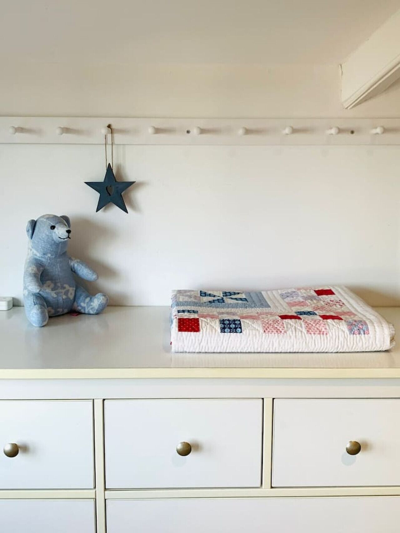 Een witte dressoir met lades, een blauwe ster decoratie en een gebogen deken.