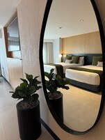 A modern hotel room with a large bed, bedside tables, and a mirror reflecting the room.