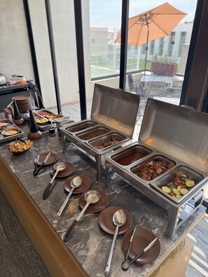 Ein reichhaltiges Buffet mit mehreren Speiseauslagen, Serviertabletts und Besteck auf einer Marmorplatte.