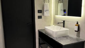 A modern bathroom with a black door, a white sink, a mirror, and a towel rack.