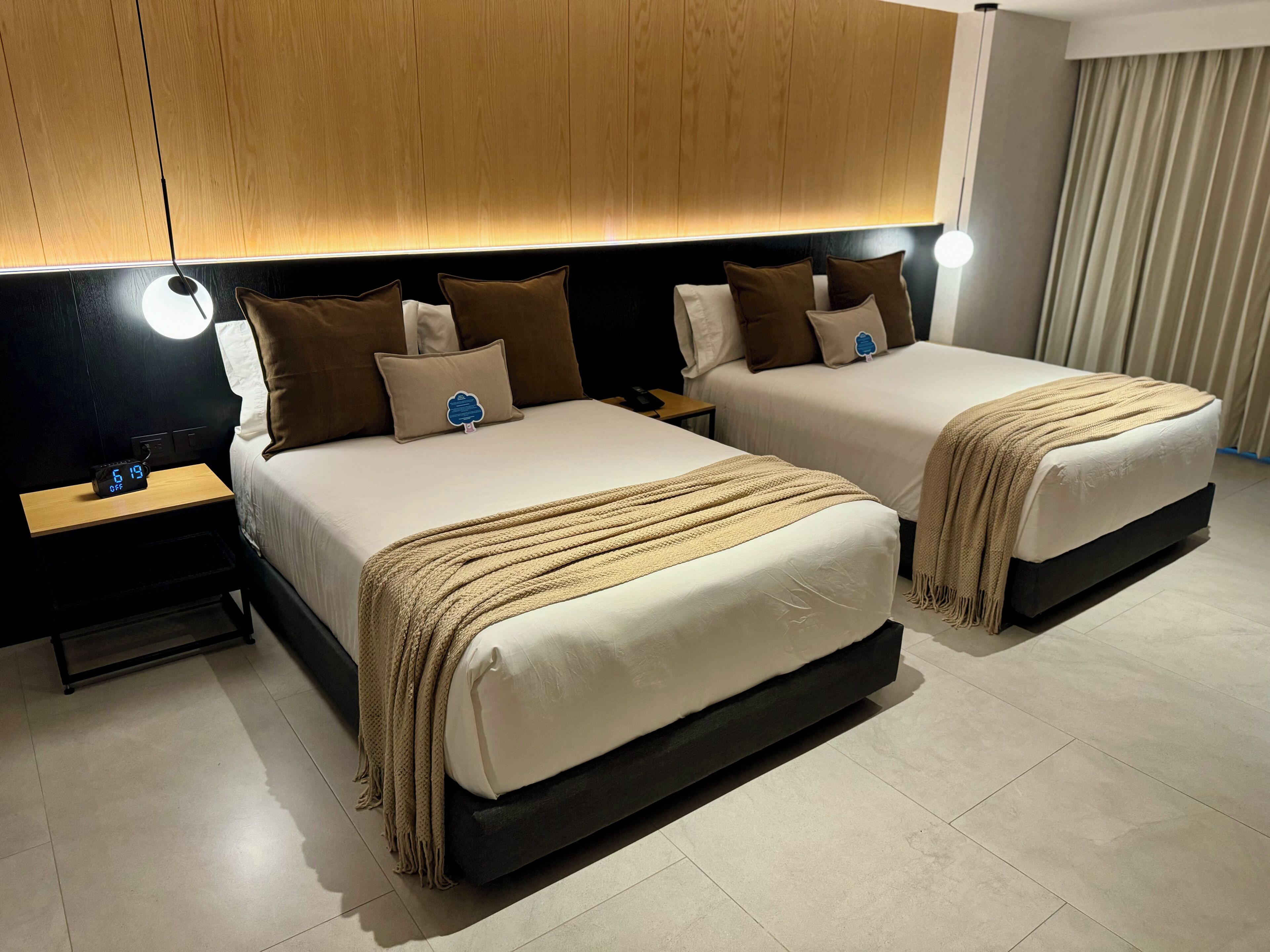 A hotel room with two beds, a nightstand with a clock, and a wooden headboard.