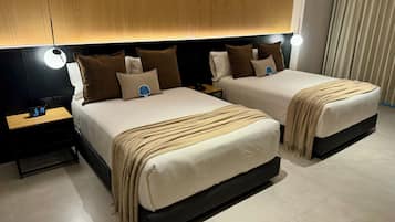 Habitación de hotel con dos camas, una mesita de noche con un reloj y un cabecero de madera.