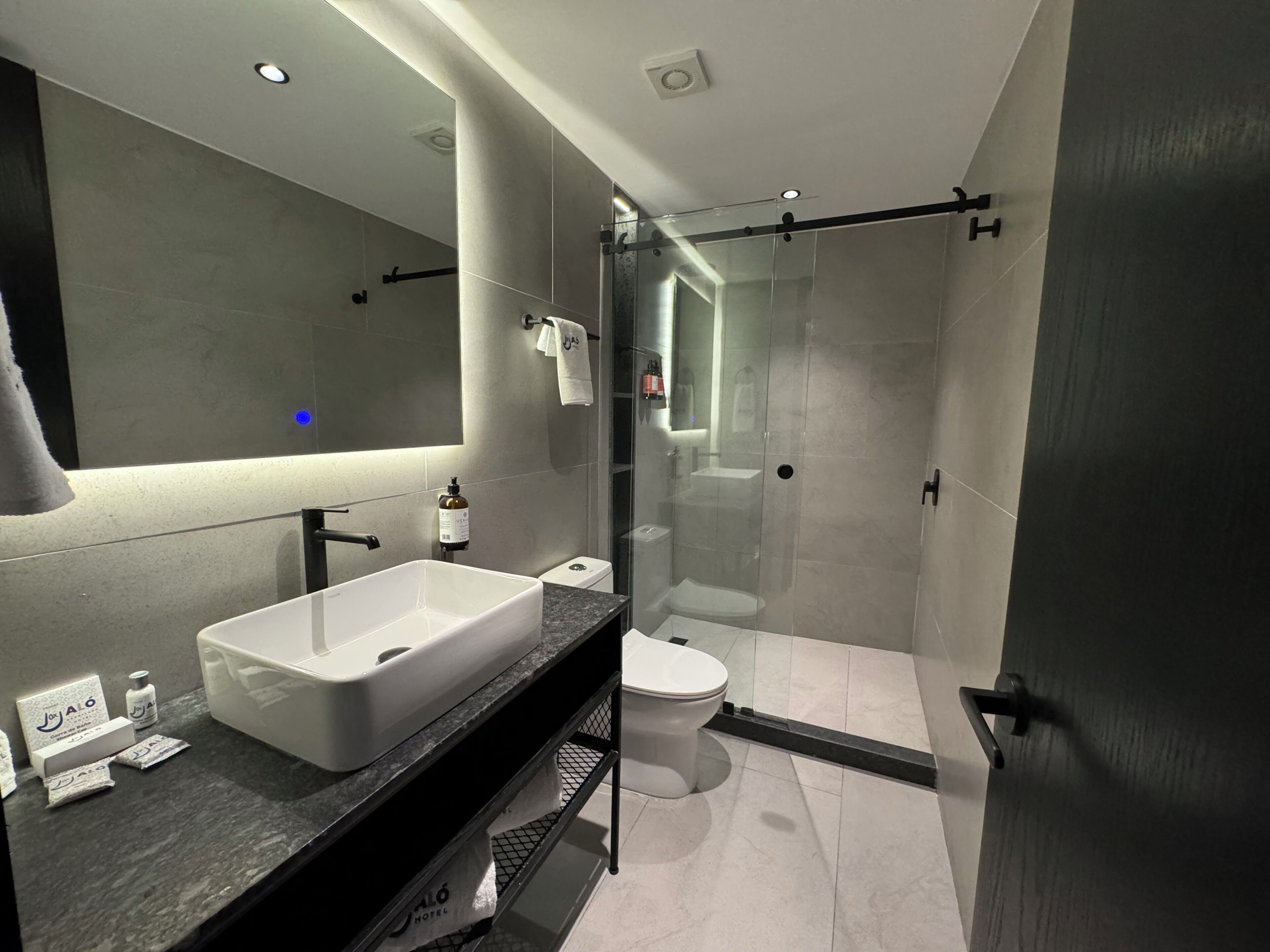 A modern bathroom with a large mirror, a white sink, a toilet, and a glass-enclosed shower area.