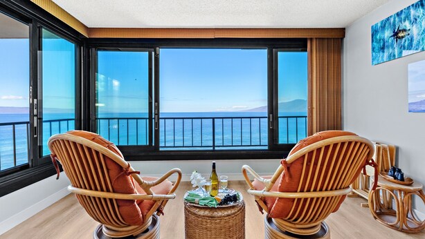 Ein Balkon mit Korbstühlen, einem kleinen Tisch mit Flasche und Gläsern und Blick aufs Meer.