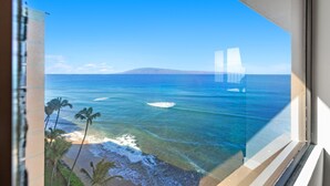 Blick aus einem Fenster auf einen Strand mit Palmen und dem Meer.