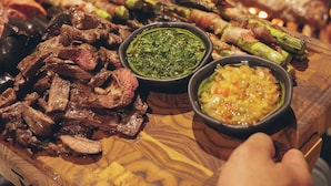 Una tabla de madera con diversas carnes y dos recipientes de salsas.