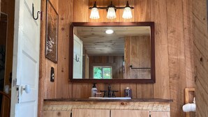 A wooden bathroom with a large mirror, three light fixtures above the sink, and a white door.