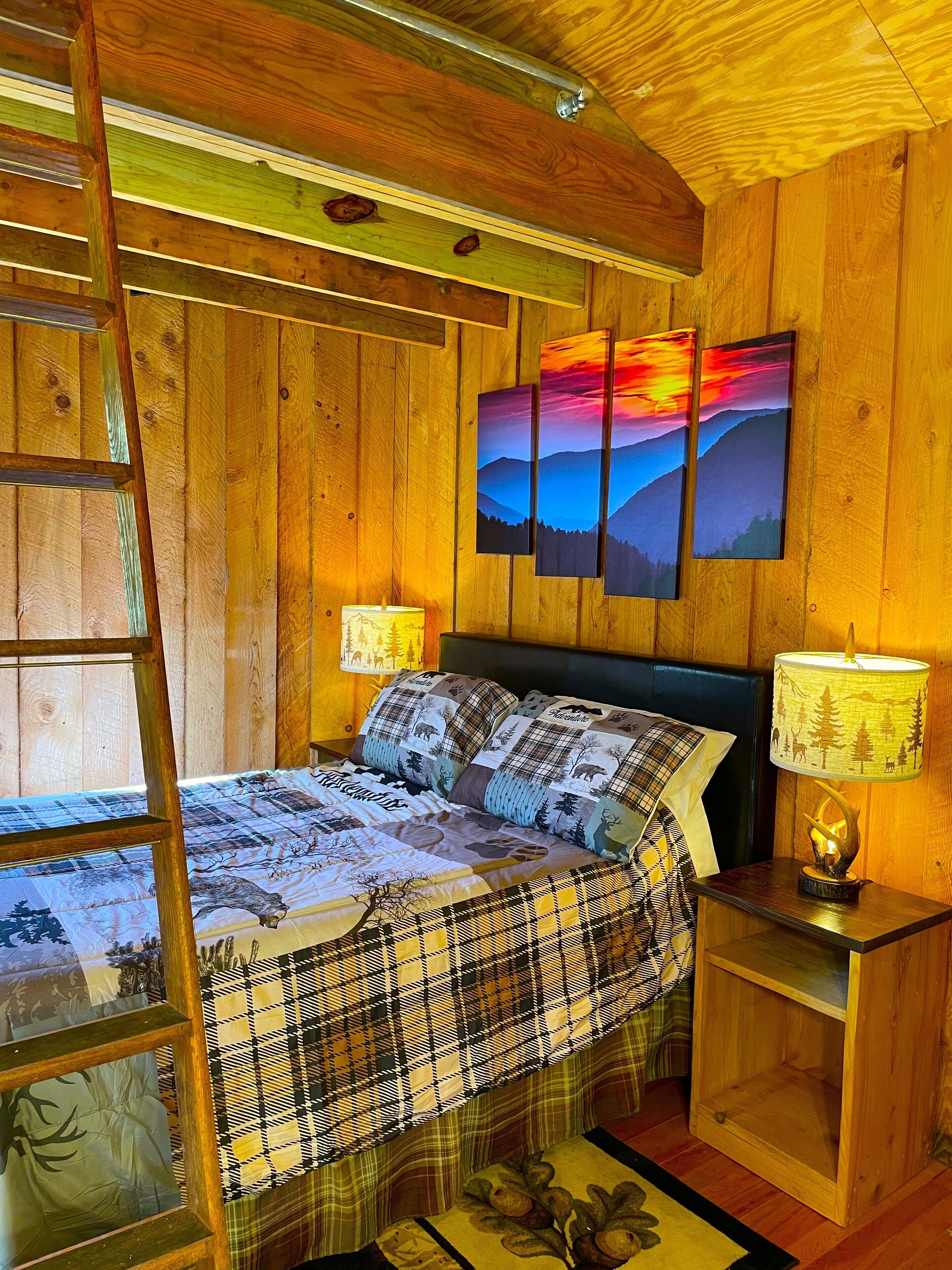 A wooden cabin bedroom with a bed, a nightstand, a lamp, and a ladder.