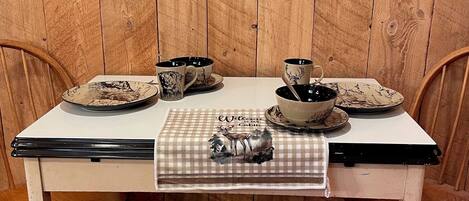A rustic wooden dining table with a map on the wall above, a checkered placemat with a deer design, and two chairs.