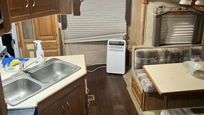 A compact RV kitchen with wooden cabinets, a sink, a small refrigerator, and a dining area with a table and cushioned seating. - Cozy mobile home  (Miami Gardens)