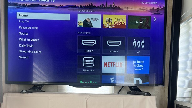 A Roku TV with a cityscape background, a white tablecloth, and a white appliance below it. - Cozy mobile home  (Miami Gardens)