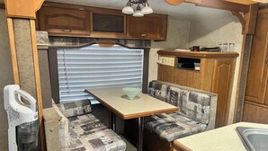 A compact RV kitchen with a dining area, including a table, bench seating, and a sink. - Cozy mobile home  (Miami Gardens)