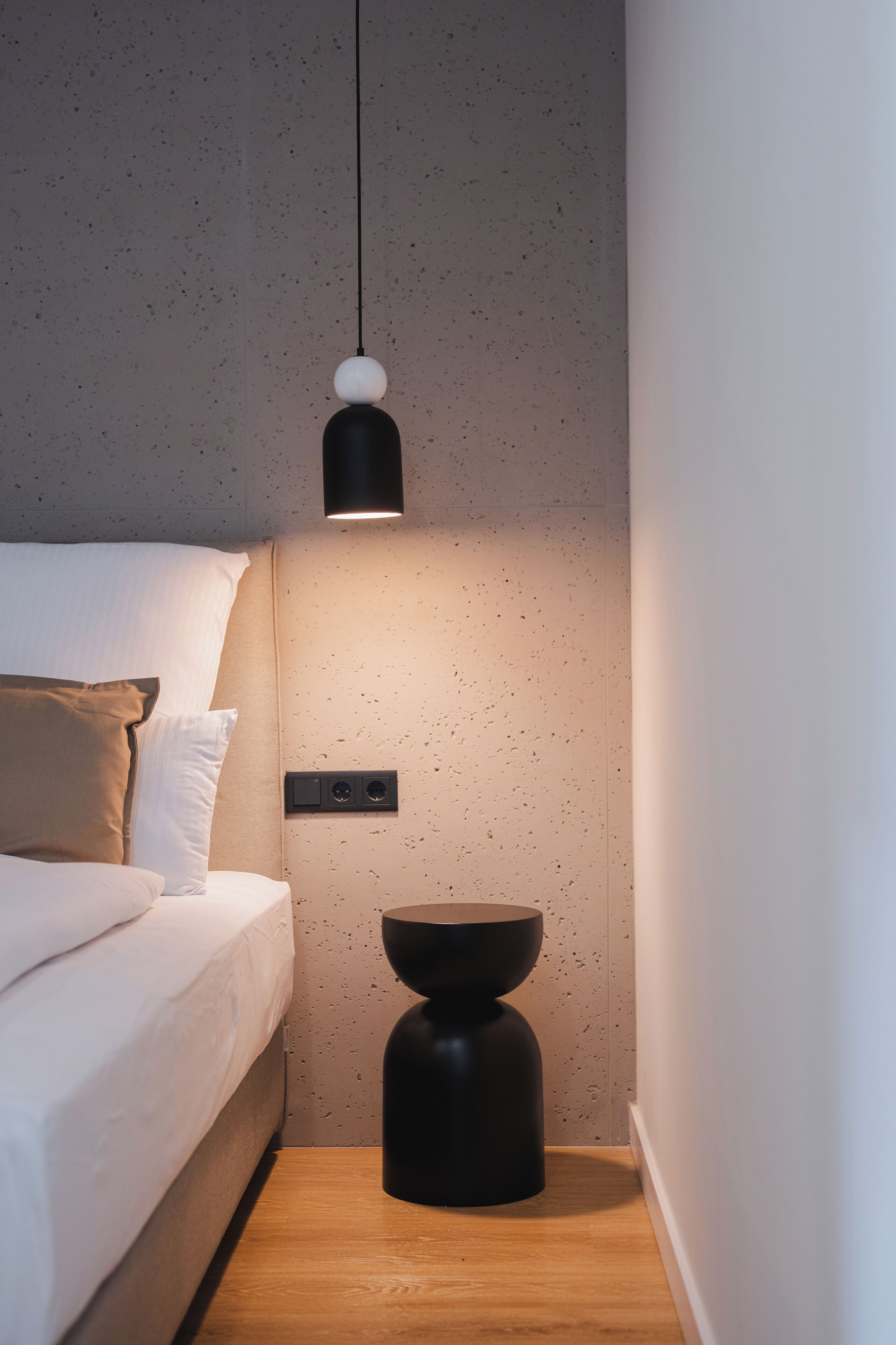 A modern bedroom with a bed, a bedside table, and a pendant light.
