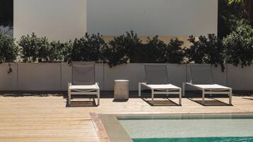 Un área junto a la piscina con dos sillones de descanso y un cubo de basura pequeño.
