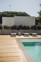 Un área junto a la piscina con dos sillones de descanso y un cubo de basura pequeño.