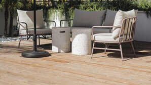 Une terrasse extérieure dotée d’un plancher en bois, de deux chaises, d’une table et d’un grand parasol offrant de l’ombre.