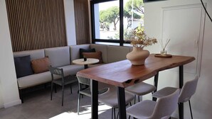 Un intérieur moderne avec une table à manger en bois, des chaises à revêtement gris, un canapé gris agrémenté de coussins, une petite table ronde et un vase contenant des fleurs séchées.