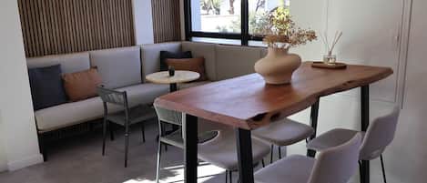 A modern interior with a wooden dining table, grey upholstered chairs, a grey sofa with cushions, a small round table, and a vase with dried flowers.