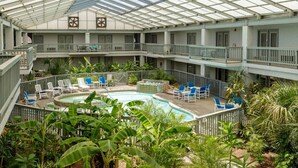 A multi-level indoor pool area with lounge chairs and a glass ceiling. - Stay Salty @ Nautilus Galleria | Heated Pool (Corpus Christi)
