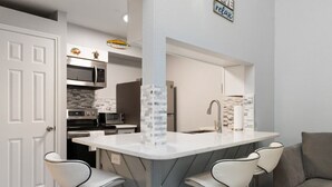 A modern kitchen with a central island, bar stools, a microwave, and a refrigerator. - Stay Salty @ Nautilus Galleria | Heated Pool (Corpus Christi)