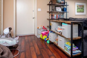 A room with a wooden floor, a baby changing station, a bookshelf with books and a framed picture, and a couch. - Spacious 3-Bedroom, 1.5-Bath Home in Central Maryland with Screened Porch & More (Severn)
