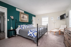 A bedroom with a bed, a chair, a dresser, and a TV on the wall. - Spacious 3-Bedroom, 1.5-Bath Home in Central Maryland with Screened Porch & More (Severn)
