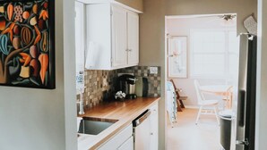 A kitchen with white cabinets, a coffee maker, and a dining area with a white chair. - Spacious 3-Bedroom, 1.5-Bath Home in Central Maryland with Screened Porch & More (Severn)