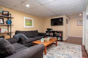 A living room with a sofa, a coffee table, a bookshelf, and a flat-screen TV mounted on the wall. - Spacious 3-Bedroom, 1.5-Bath Home in Central Maryland with Screened Porch & More (Severn)