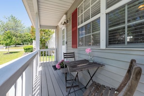 A covered porch with a table and chairs, a potted plant, and a window with shutters.