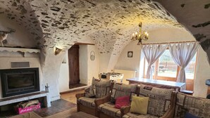 A rustic interior with a fireplace, sofa set, wooden table, and a view of the outdoors. - Large family home in the mountains with swimming pool  (Faucon-de-Barcelonnette)