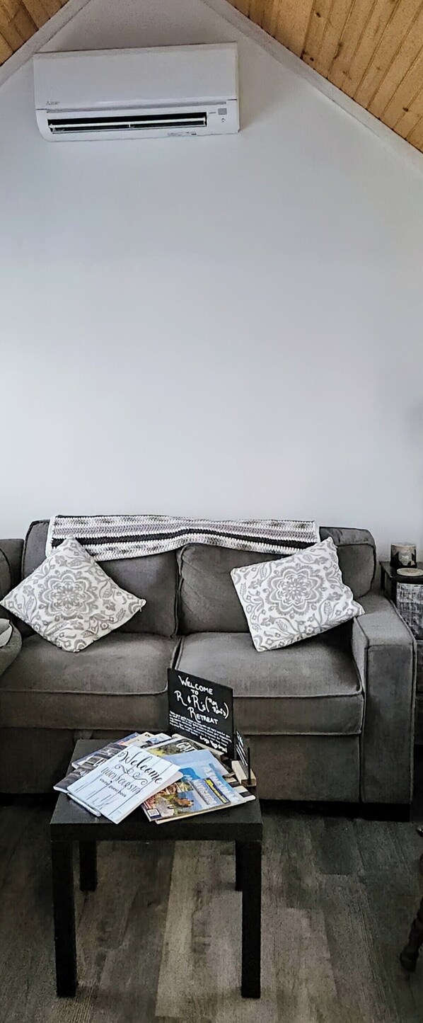 A living room with a grey sofa, patterned cushions, a small coffee table with magazines, and a welcome sign. - R & R's Modern Retreat (Newport)