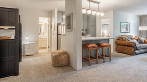 Una sala de estar moderna con un espejo grande, una zona de cocina y un área de descanso con un sofá y dos sillones.