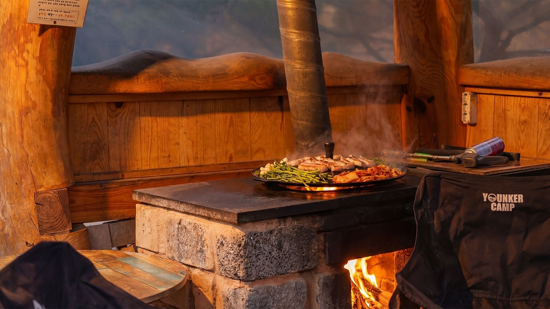 Ein Grill mit Holzfeuer, ein Steinofen und eine 'YOUNKER CAMP' Tasche.