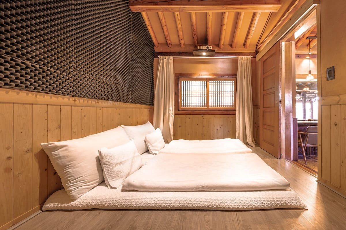 A cozy wooden room with a bed, a window with curtains, and a wooden ceiling.