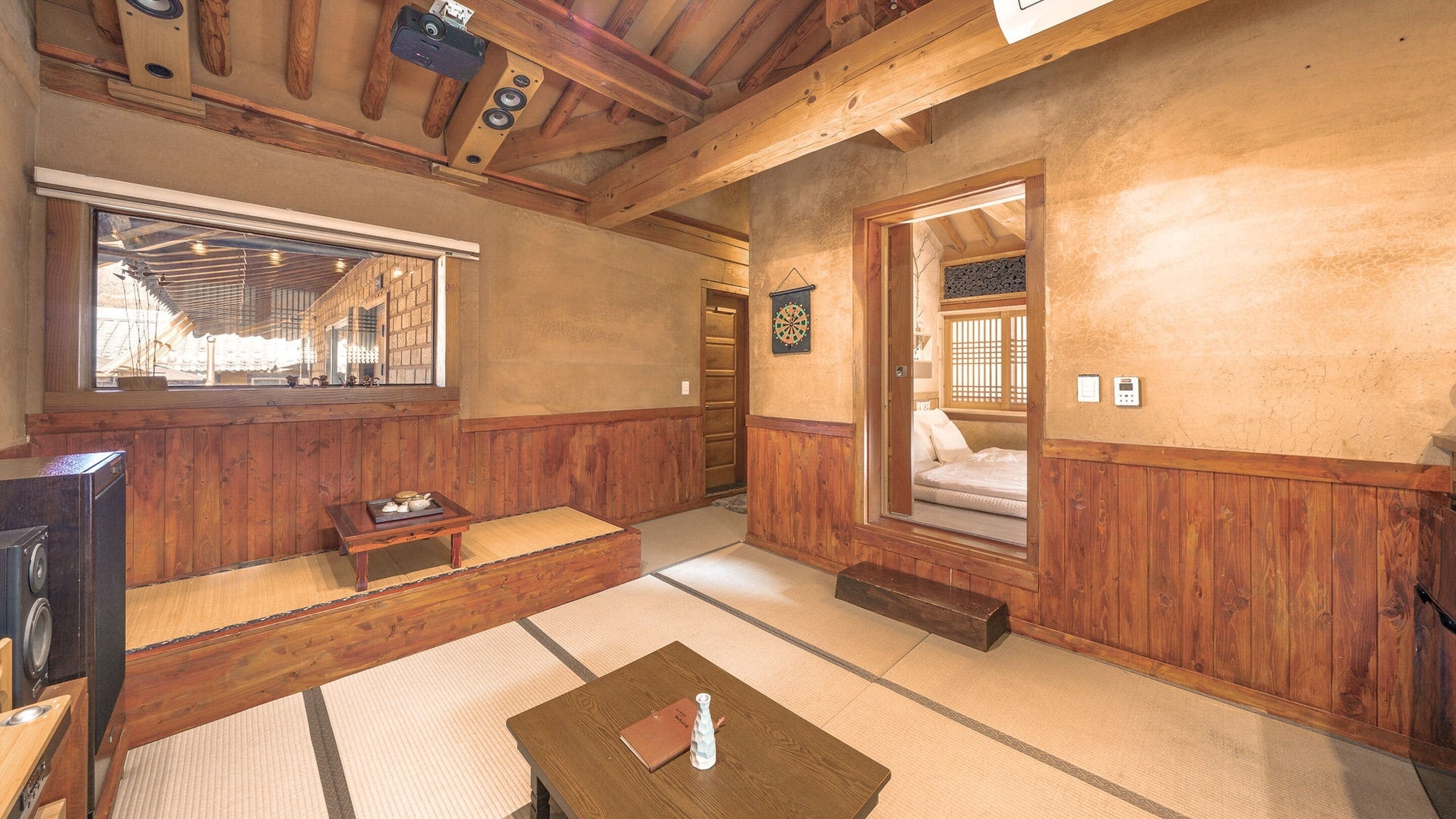 A traditional Japanese-style room with tatami flooring, a futon bed, a television, and a small table with a bottle and a book.